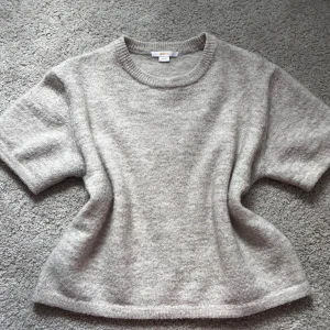 Beige stickad kortärmad tröja - Mysig beige stickad tröja med korta ärmar och rund halsringning. Tröjan har en rak passform och är perfekt för lager-på-lager-stil. Enkel och stilren design som passar till mycket.