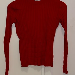 Röd ribbad tröja från H&M - Säljer en röd ribbad långärmad tröja från H&M Basics. Tröjan har en tight passform och är tillverkad i ett stretchigt material som sitter snyggt på kroppen. Perfekt att styla med jeans eller kjol.