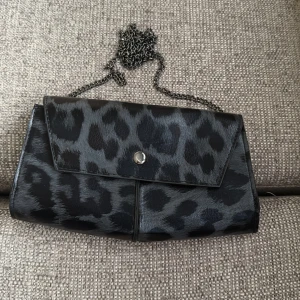 Svart leopardmönstrad axelväska med kedja - Snygg svart kuvertväska med leopardmönster och silverfärgad kedja. Väskan har magnetlås och insidan är fodrad med klassiskt rutigt tyg. Bara att skriva vid frågor och priset kan såklart diskuteras!