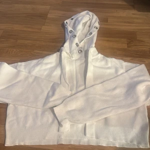 Vit hoodie från ZARA med silverdetaljer - Säljer en vit hoodie från ZARA med långa ärmar och croppad passform. Huvan har snygga silverfärgade öljetter och tröjan är stickad med breda muddar vid ärmslut och nederkant. Perfekt för en stilren och avslappnad look.
