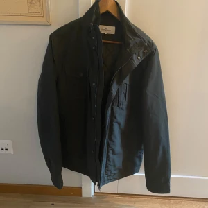 Grön jacka från John Henric  - Stilren grön jacka från John Henric med hög krage och två bröstfickor med lock. Jackan har dragkedja och knappar framtill. Nypris 1499kr