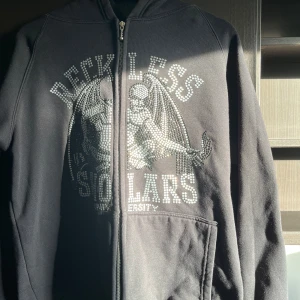 Reckless Scholars Zip Hoodie - Reckless Scholars Zip Hoodie i svart. I bra skick! Saknar enbart två nitar och färgen har avtagit på vissa, se bilder.