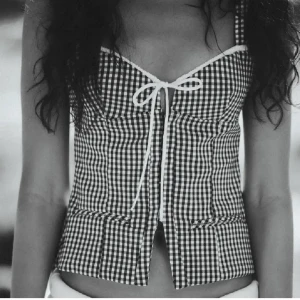 Svartvit rutig korsettopp med knyt - Snygg korsettopp i svartvitt rutigt mönster med smala axelband och knyt framtill. Toppen har en figurnära passform och markerad byst. Perfekt för att skapa en trendig look. Den är från Zara och har använt den fåtal gånger!❤️❤️❤️