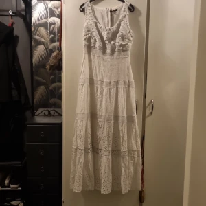 Vit spetsklänning från Sheilay - Romantisk vit långklänning från Sheilay med vackra spetsdetaljer och broderier. Klänningen är ärmlös och har en feminin, luftig passform med volang upptill. Perfekt för sommarens alla tillfällen. PRIS:500KR