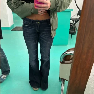 Mörkblå bootcut jeans - Säljer ett par mörkblå jeans med bootcut passform och låg midja. Jeansen har klassisk femficksdesign och stängs med dragkedja och knapp. Perfekta för dig som gillar en retroinspirerad look.