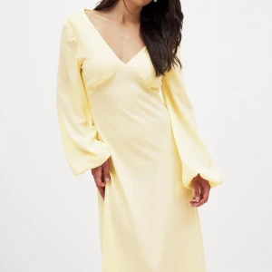 Ljusgul långklänning med v-ringning och öppen rygg - Superfin ljusgul långklänning från NA-KD med v-ringad hals, långa vida ärmar och öppen rygg med knytband. Perfekt för sommarens tillfällen när du vill sticka ut med en elegant och luftig look.