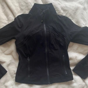 Define Cropped JacketNulu lululemon  - Säljer en svart, figursydd träningsjacka från Lululemon med hög krage och hel dragkedja framtill. Jackan har långa ärmar och två fickor med dragkedja. Perfekt för träning eller som ett sportigt lager. Använd endast 1 gång!! Köpte på lululemon butiken på NK på Östermalm🥰höjde precis priset för jag råkade skriva in fel..😌