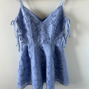 Ljusblå spetsklänning från Miss Selfridge - Supersöt ljusblå kortklänning från Miss Selfridge i spets med smala axelband och knytband på sidorna. Klänningen har v-ringning och är helfodrad, perfekt för sommarens alla tillfällen.