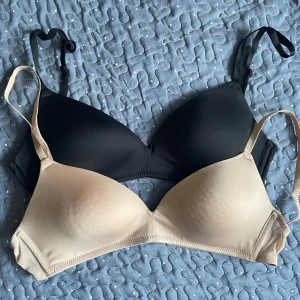 2-pack BH i svart och beige - Säljer två stilrena BH:ar från H&M, en i svart och en i beige. Båda har justerbara axelband och slät, vadderad kupa utan synliga sömmar. Perfekta under alla typer av toppar för en osynlig look.