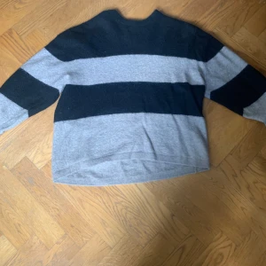 Grå och svart randig stickad tröja från & Other Stories - Mysig stickad tröja från & Other Stories i beige och svart med breda ränder. Tröjan har lång ärm och en avslappnad passform, perfekt för kyligare dagar.