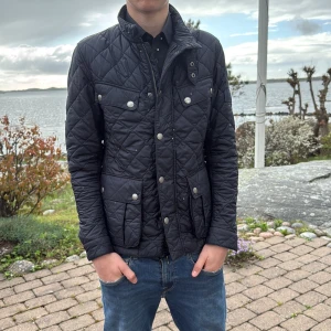 Svart quiltad jacka från Barbour - Stilren svart quiltad jacka från Barbour med hög krage, tryckknappar och dragkedja. Flera fickor framtill och diskret Barbour-logga på insidan. Perfekt för kyliga dagar och enkel att matcha med jeans.                                                                           endast använd 3 gånger ! 