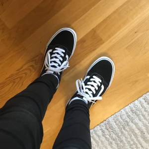 Vans - Klassiska svarta Vans sneakers med vit sula och vita skosnören. Skorna har en låg profil och rund tå, perfekt för en avslappnad stil. Passar till det mesta och är riktigt bekväma att gå i.