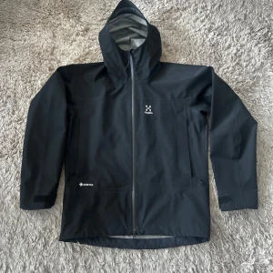 Svart skaljacka från Haglöfs - Säljer min svarta Haglöfs skaljacka då jag inte längre använder den. Jackan är i toppen skick men endast lite defekter på huvan, bara använd 1 säsong. Modellen heter Spire GTX Jacket och nypris låg på 5000kr. Bara skriva vid frågor!
