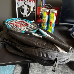 Svart Wilson tennis väska plus rack - Säljer en svart tennisväska från Wilson med dragkedja. Väskan har plats för racket och tillbehör, perfekt för att ta med till tennisbanan. Snygg och sportig design med Wilson-logga på sidan.