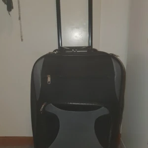 Svart resväska med hjul och teleskophandtag - Säljer en svart resväska med två hjul och teleskophandtag. Väskan har ytterfack med dragkedja och ett stort huvudfack med spännband på insidan. Perfekt för resor och enkel att rulla med sig.