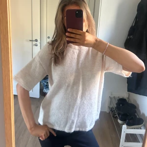 Vit stickad tröja med kort ärm - Säljer en vit stickad tröja med korta ärmar och rund hals. Tröjan har en avslappnad passform.