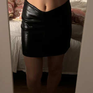 Svart skinnkjol - Säljer en svart kort skinnkjol med tight passform. Kjolen har en stilren och minimalistisk design utan synliga detaljer. Perfekt för dig som gillar en edgy och trendig look.