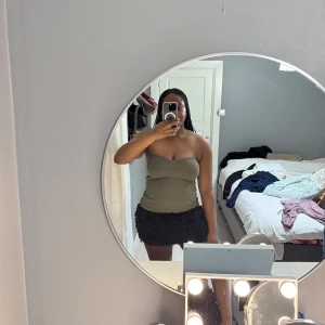 Olivgrön ribbad tubtopp - Säljer en olivgrön ribbad tubtopp med en lätt hjärtformad överkant. Toppen är ärmlös och har en tight passform, perfekt att styla till olika outfits. Superenkel och snygg att bära till både jeans och kjol.