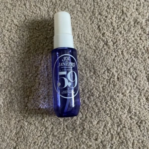 Sol de Janeiro Parfymmist 59 - En snygg parfymmist från Sol de Janeiro i en genomskinlig lila plastflaska med vit spraykork. Flaskan har tryckt text och siffran 59 på framsidan. Perfekt att ta med i väskan för en fräsch doft när som helst.