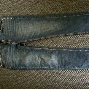 Blå jeansbyxor från 157 - Klassiska blå jeansbyxor från 157 med raka ben och femficksdesign. Jeansen har orangea sömmar och en läderpatch bak i midjan. Perfekta för dig som gillar en tidlös och enkel stil.