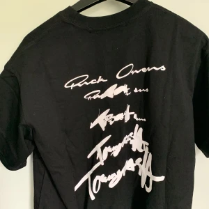 Svart t-shirt från Rick Owens x Tommy Cash - Säljer en svart t-shirt från Rick Owens i samarbete med Tommy Cash. T-shirten har vit grafisk text på både fram- och baksidan samt en klassisk rund halsringning. Storleken är S men passar mer M.