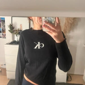 Svart stickad tröja från Calvin Klein Jeans - Säljer en svart stickad tröja från Calvin Klein Jeans med vit CK-logga på bröstet. Tröjan har rund halsringning.