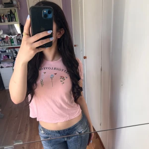 Ljusrosa croppad t-shirt med blommor från H&M Divided - Säljer en ljusrosa croppad t-shirt från H&M Divided med tryck av blommor och texten 'Best of love'. T-shirten har korta ärmar och är i mjuk bomull, perfekt till jeans eller shorts.