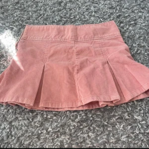 Rosa manchesterkjol från Gina Tricot - Supersöt rosa minikjol i manchester från Gina Tricot. Kjolen har veckade detaljer och dragkedja i sidan. Perfekt för dig som vill ha en trendig och bekväm kjol!