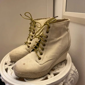 Beiga kilklackade boots från Din Sko - Snygga boots i beige canvas från Din Sko med kilklack och flätad detalj runt sulan. Skorna har snörning med olivgröna skosnören och rund tå. Perfekta för dig som vill ha en cool och avslappnad stil med lite höjd.