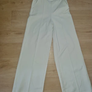 Vita wide byxor från Gina Tricot XS - Snygga vita byxor från Gina Tricot i storlek XS. Byxorna har en wide passform med hög midja och raka ben. Tillverkade i ett strukturerat tyg som ger en cool känsla. Perfekta att styla med crop top eller oversized hoodie.