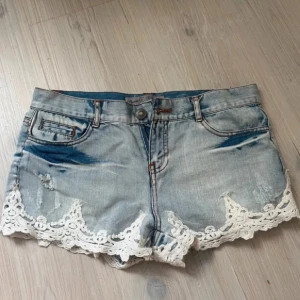 Jeansshorts med spets från Denim Co. - Snygga ljusblå jeansshorts från Denim Co. med slitna detaljer och vit spetskant längst ner. Klassisk femficksmodell med knapp och dragkedja framtill. Perfekta för sommaren! Står att de är stolen 40 men är mycket mer en liten 38 eller 36