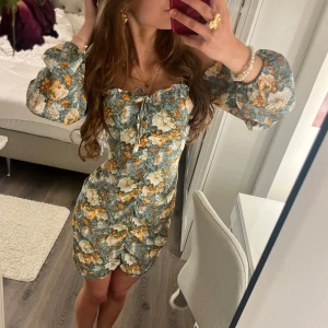 Blommig klänning med puffärmar - Superfin kortklänning med blå botten och blommigt mönster i vitt, gult och grönt. Älskar den här klänningen den är super fin och har en dold dragkedja så man lätt kan få på sig den💗Skriv om du har fler frågor🫶