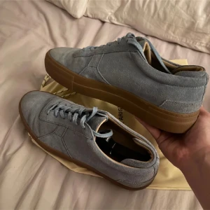 Blå mockasneakers från Axel Arigato - Snygga sneakers i ljusblå mocka från Axel Arigato med bruna gummisulor. Skorna har klassisk rund tå, platt sula och snörning framtill. Perfekta för dig som gillar stilrena och trendiga sneakers med premiumkänsla. Har boxen till