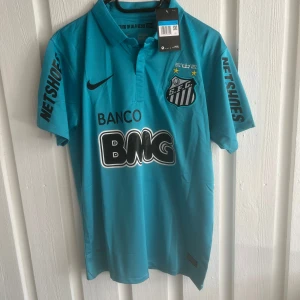 Santos Neymar Jr Nike fotbollströja blå - Santos FC matchtröja i blått med Neymar Jr och nummer 11 på ryggen. Tröjan har korta ärmar, tryckta sponsorer och klubbmärke på bröstet. Tillverkad i lätt och ventilerande material, perfekt för fotbollsplanen eller att bära som supporter.