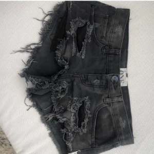 Svarta slitna jeansshorts ONE - Riktigt snygga svarta jeansshorts från ONE med rejält slitna detaljer och fransiga kanter. Modellen är kort och har hög midja, perfekt för en edgy streetstyle. Gjorda i denim med coola hål och råa avslut. Passar dig som vill sticka ut i sommar!