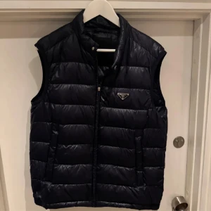 Mörkblå dunväst från Prada - Snygg mörkblå dunväst från Prada i storlek S med dragkedja och två fickor framtill. Dragkedjaöglan har lossnat men medföljer och kan enkelt sättas tillbaka. PRIS KAN DISKUTERAS VID SNABB AFFÄR!!!!!!