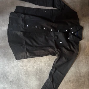 Svart skjorta från Ralph Lauren L - Klassisk svart skjorta från Ralph Lauren i storlek L. Skjortan har vit broderad logga på bröstet, vita knappar och button down-krage. Tillverkad i bomull och har lång ärm. Perfekt för en clean och stilren look. Passar d och M