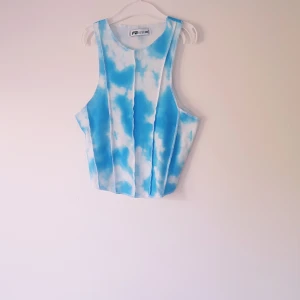 Blåvit ribbad linnetopp FB Sister - Superfräsch ribbad linnetopp från FB Sister i blått och vitt tie-dye mönster. Toppen är ärmlös med breda axelband och har en croppad passform. Perfekt för varma dagar och ger en chill vibe till din outfit.   Helt skick dock finns obehandlade fläckar