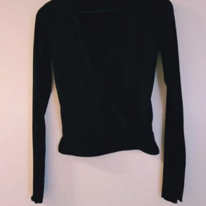 Svart omlottopp från NA-KD XS - Snygg svart omlottopp från NA-KD i storlek XS. Toppen har lång ärm, v-ringning och är ribbad för en extra stilren look. Perfekt att matcha med jeans eller kjol för en trendig outfit.  Helt & fint skick