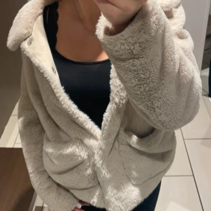 Beige teddyjacka med stora fickor - Supermjuk och fluffig beige teddyjacka med stora framfickor och knäppning framtill. Jätte fin till hösten 