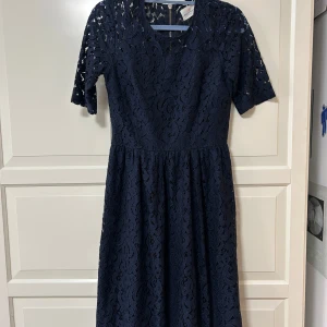 Marinblå spetsklänning  - Snygg marinblå klänning i spets med halvärmade ärmar och rund halsringning. Klänningen har en markerad midja, lätt utställd kjol och dragkedja i ryggen. Framhäver kurvor, snyggaste klänningen jag haft, men är för liten för meg dessverre