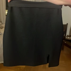 Svart kortkjol med slits - Enkel och stilren svart kortkjol med liten slits framtill. Kjolen har rak passform och bred midja, perfekt för att skapa en clean look. Materialet känns mjukt och stretchigt, vilket gör den bekväm att bära hela dagen.