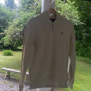 Beige half zip tröja från Gant - Snygg beige långärmad tröja från Gant med halv dragkedja och broderad logga på bröstet. Klassisk och stilren modell med ribbade muddar och hög krage. Perfekt för lager-på-lager och passar till det mesta. använd några gånger men skicket är som nytt! Hör av dig vid frågor/ funderingar 