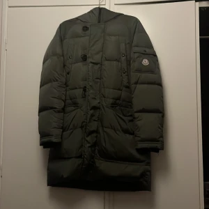 moncler jacka - Säljer en grön Moncler dunjacka med pälsdetalj på huvan . Jackan har stora fickor, knappar och dragkedja framtill samt Moncler-logga på ärmen. Perfekt för kalla dagar och det går att ta av pälsen.vintage moncler