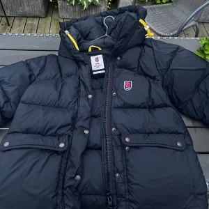 Svart Fjällräven Expedition dunjacka L - Säljer min fina fjällräven jacka som bara är använd en säsong. Jackan är i mycket bra skick och har inga skador eller fläckar. Den är varm och skön, perfekt för kalla vinterdagar. Säljer den eftersom jag behöver en annan storlek. 