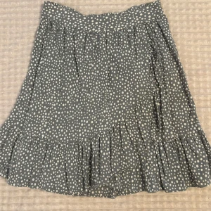 Kjol från vero moda - Supersöt kort kjol från Vero Moda i grönt med vita prickar. Kjolen har volangkant nertill och resår i midjan. Använd fåtal gånger för flera år sedan så är i princip i nyskick. 