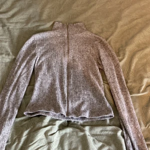 Grå ribbad ziptröja med hög krage - Grå ribbad tröja med lång ärm och hög krage. Tröjan har en dragkedja framtill som går hela vägen upp till halsen. Mjuk och stretchig, perfekt för lager-på-lager. Enkel och stilren design som funkar till många outfits.