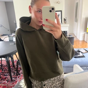 Olivgrön hoodie med huva - Säljer en olivgrön hoodie med huva och långa ärmar. Tröjan har en relaxed passform och är tillverkad i mjukt bomullsmaterial. Perfekt för chill dagar eller när du vill ha en enkel och stilren look.