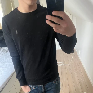 Svart merinoull tröja från Ralph Lauren - Svart långärmad tröja från Ralph Lauren med klassisk rund hals och den är i 100% merino ull och är extremt skön, sitter perfekt på mig och jag är runt 176 så är du runt där passar den dig har ett litet hål på armen 