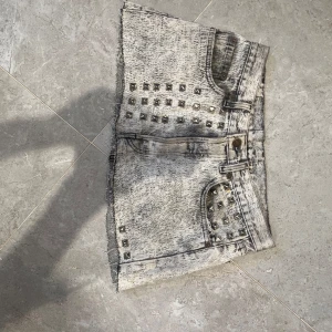 Grå jeansshorts med nitar från Levi's - Snygga grå jeansshorts från Levi's med slitna kanter och coola silverfärgade nitar på framsidan. Shortsen har klassisk femficksdesign, låg midja och en tvättad, nästan marmorerad look. Perfekta för dig som vill sticka ut med en edgy stil.